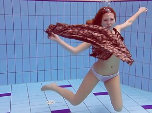 Slim redhead looker dives around the pool in the nude