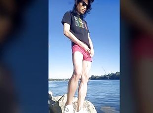 Twink boy with long dark hair pissing pee on the river dressed in g...